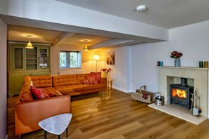 A cozy living room with a sofa, a small table, a fireplace, and a bookshelf. - The Cottages Collection at Rusty Lane Farm (Seend)