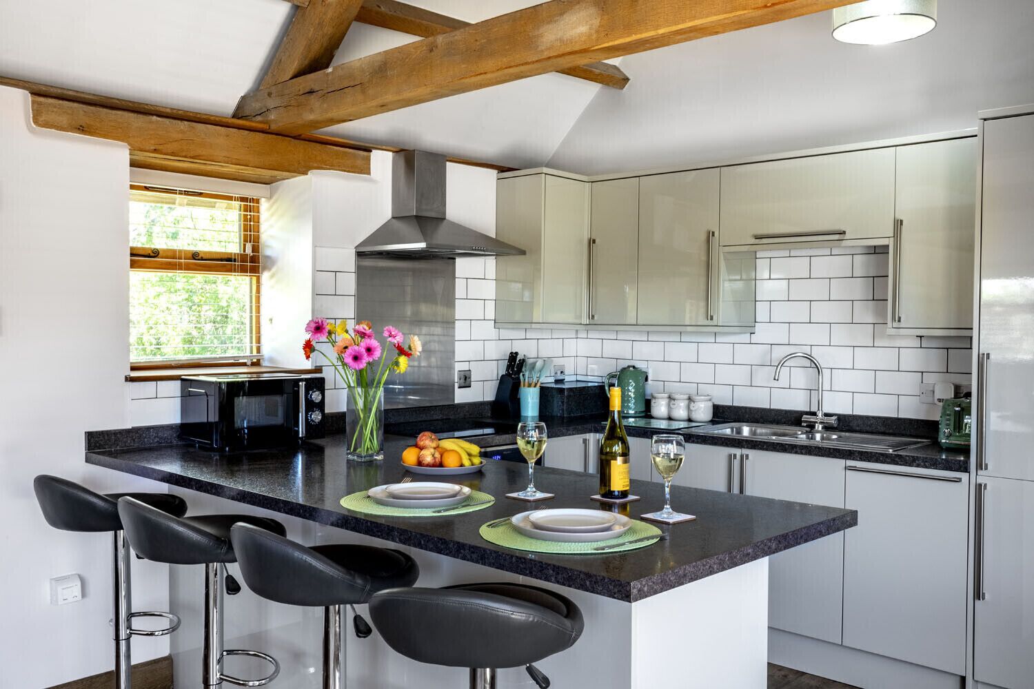Una cocina moderna con una isla central, taburetes de bar, una campana extractora de acero inoxidable y un ventanal con vistas a zonas verdes.
