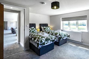 A modern bedroom with a double bed, a bedside table, a lamp, and a window with a view. - The Cottages Collection at Rusty Lane Farm (Seend)