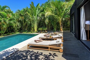 Ein Poolbereich mit Liegestühlen und einem Tisch, umgeben von üppiger tropischer Vegetation.