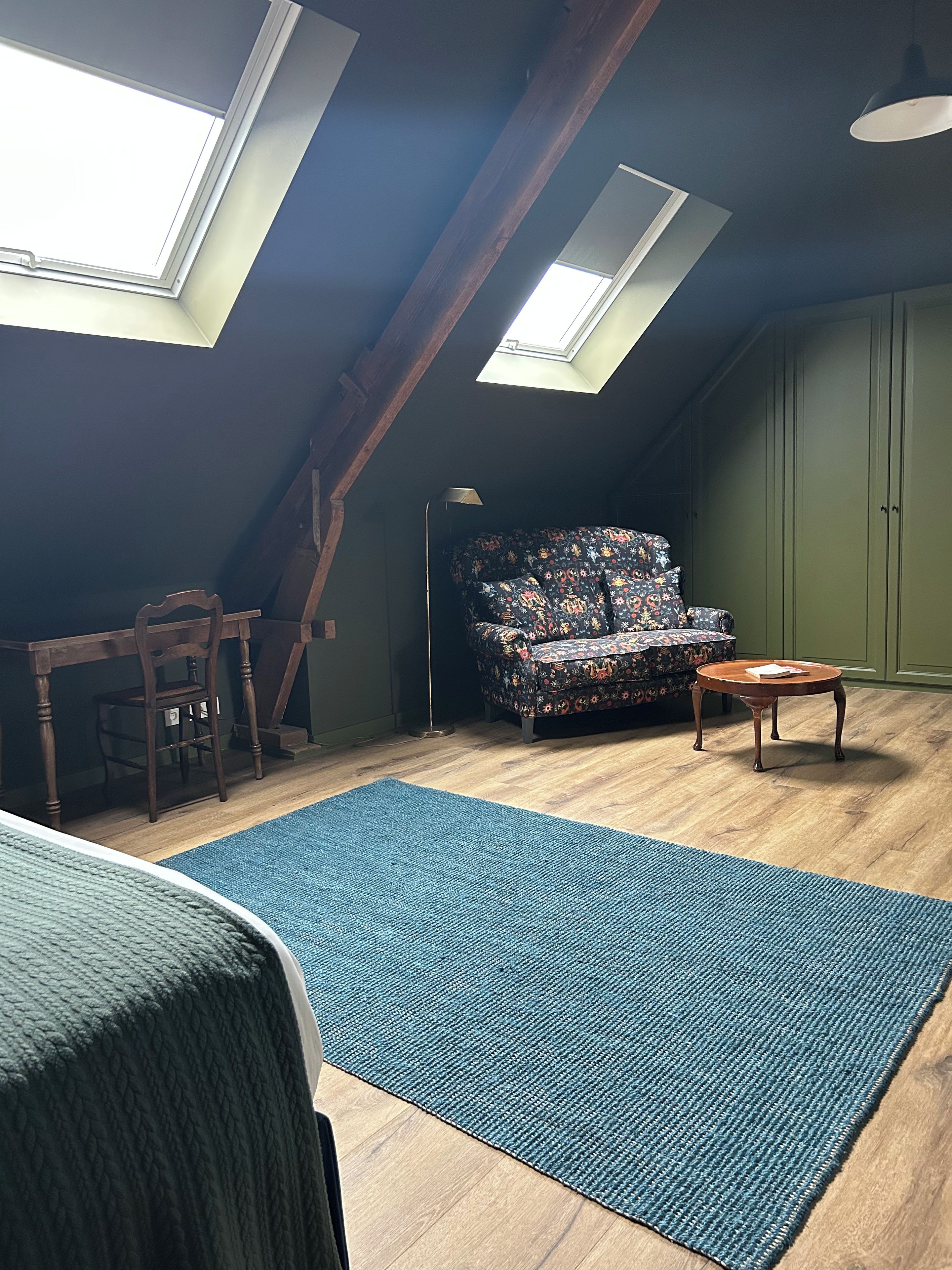 Une pièce avec un plafond en pente, un canapé, une petite table, une chaise et un tapis bleu.