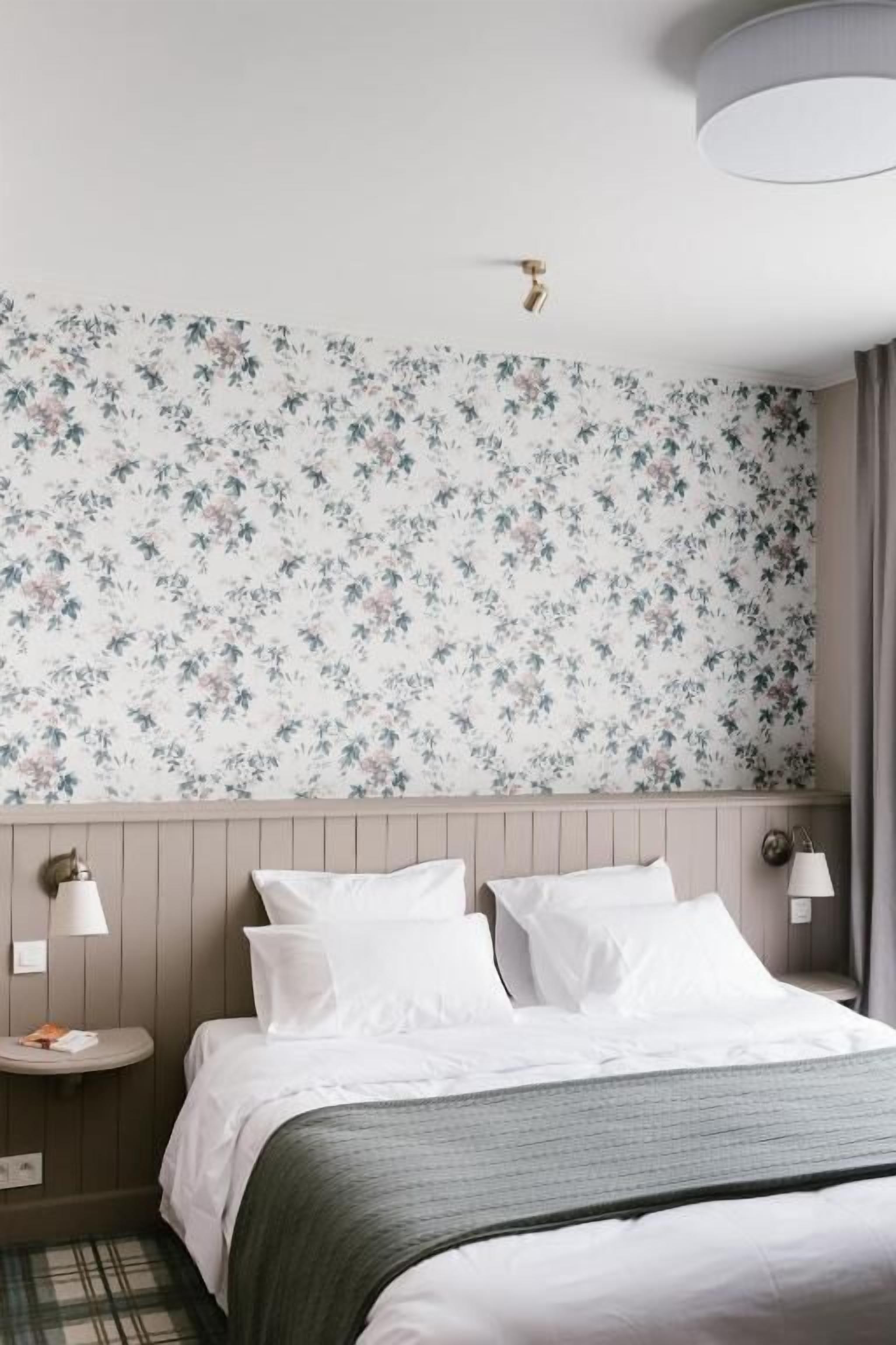 Une chambre d’hôtel avec un lit, une table de chevet, une lampe et un papier peint à motifs floraux.