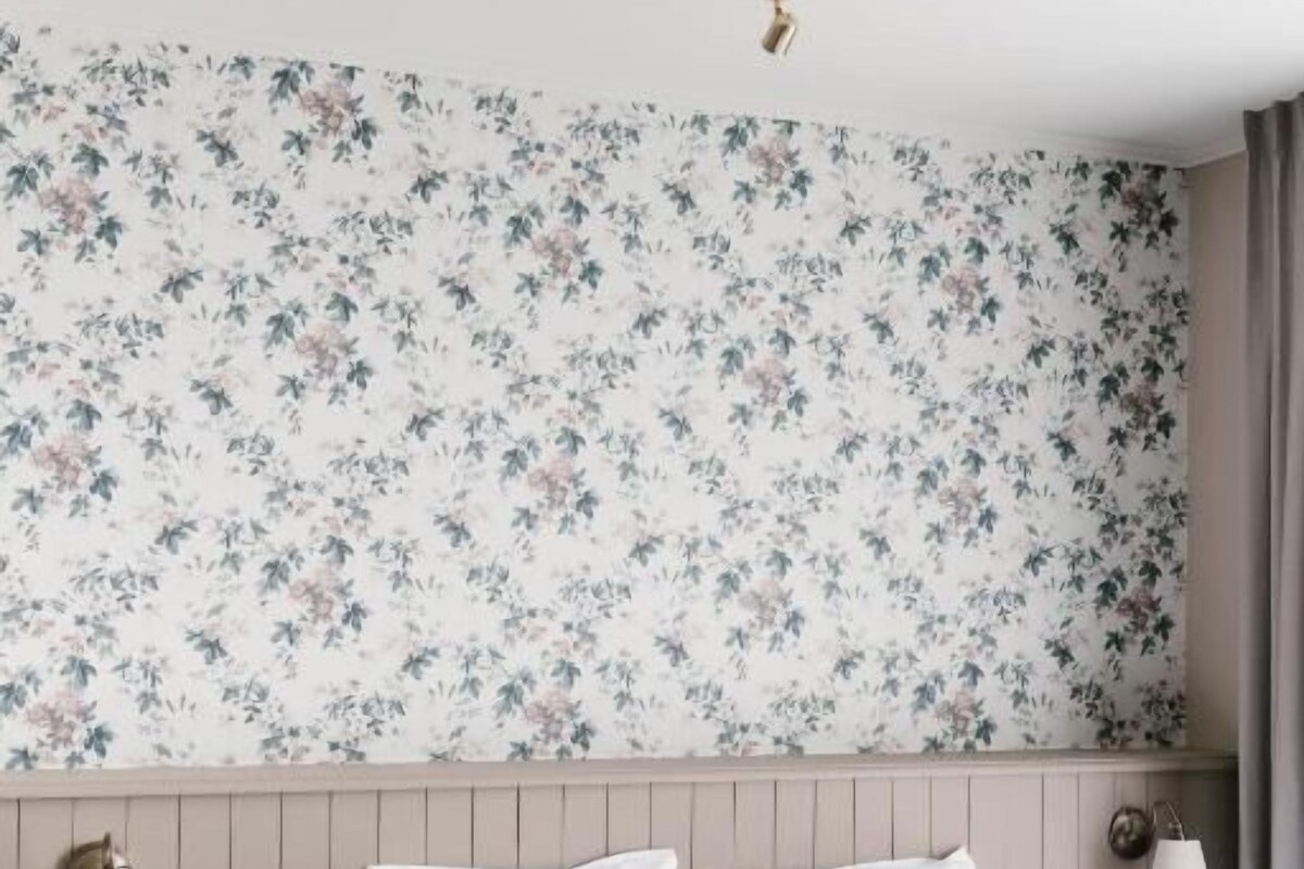 A hotel room with a bed, a nightstand, a lamp, and a floral wallpaper.