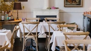 A dining area with tables set for guests, a fireplace, and wall-mounted artwork.