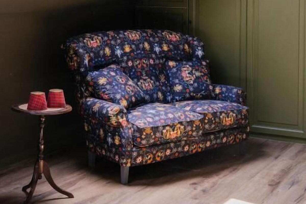 A room with a sloped ceiling, a skylight, a patterned sofa, a small round table with two red candles, and a green wall.