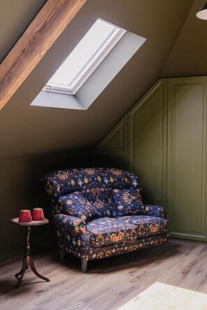 A room with a sloped ceiling, a skylight, a patterned sofa, a small round table with two red candles, and a green wall. - La Maison d'Hôtes (SILLY)