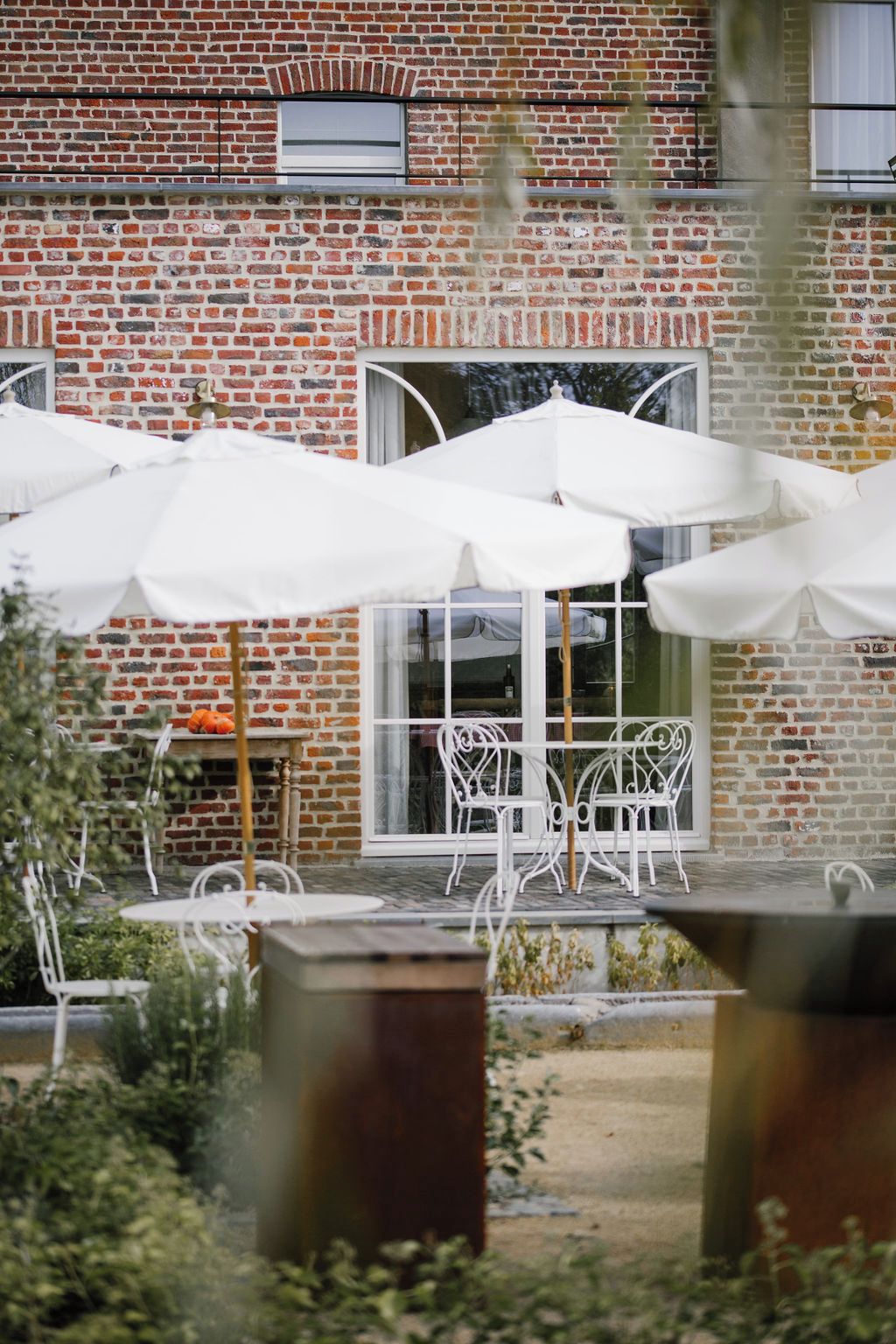 Een gebouw van baksteen met wit tuinmeubilair en parasols.