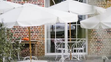 Een gebouw van baksteen met wit tuinmeubilair en parasols.