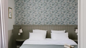 A bedroom with a bed, two bedside lamps, a nightstand, a framed picture, and a floral wallpaper.