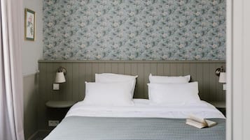A bedroom with a bed, two bedside lamps, a nightstand, a framed picture, and a floral wallpaper.