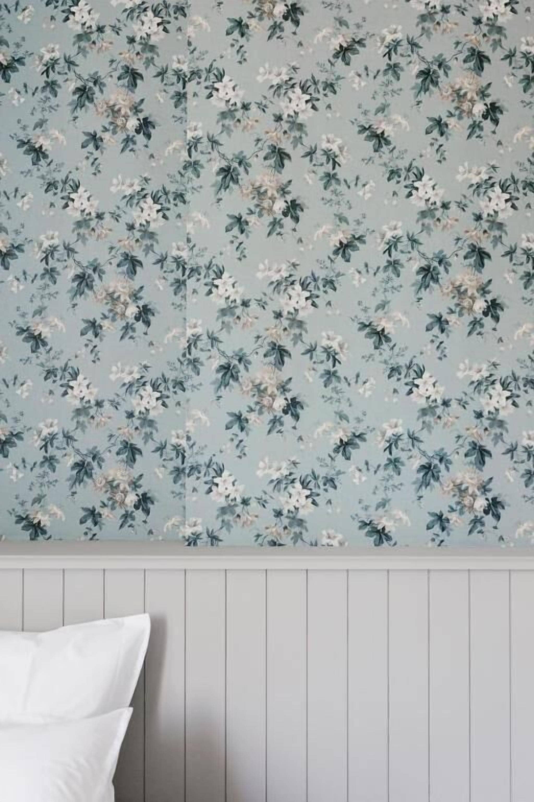 Une chambre avec un papier peint à motifs floraux et un lit blanc avec deux oreillers.