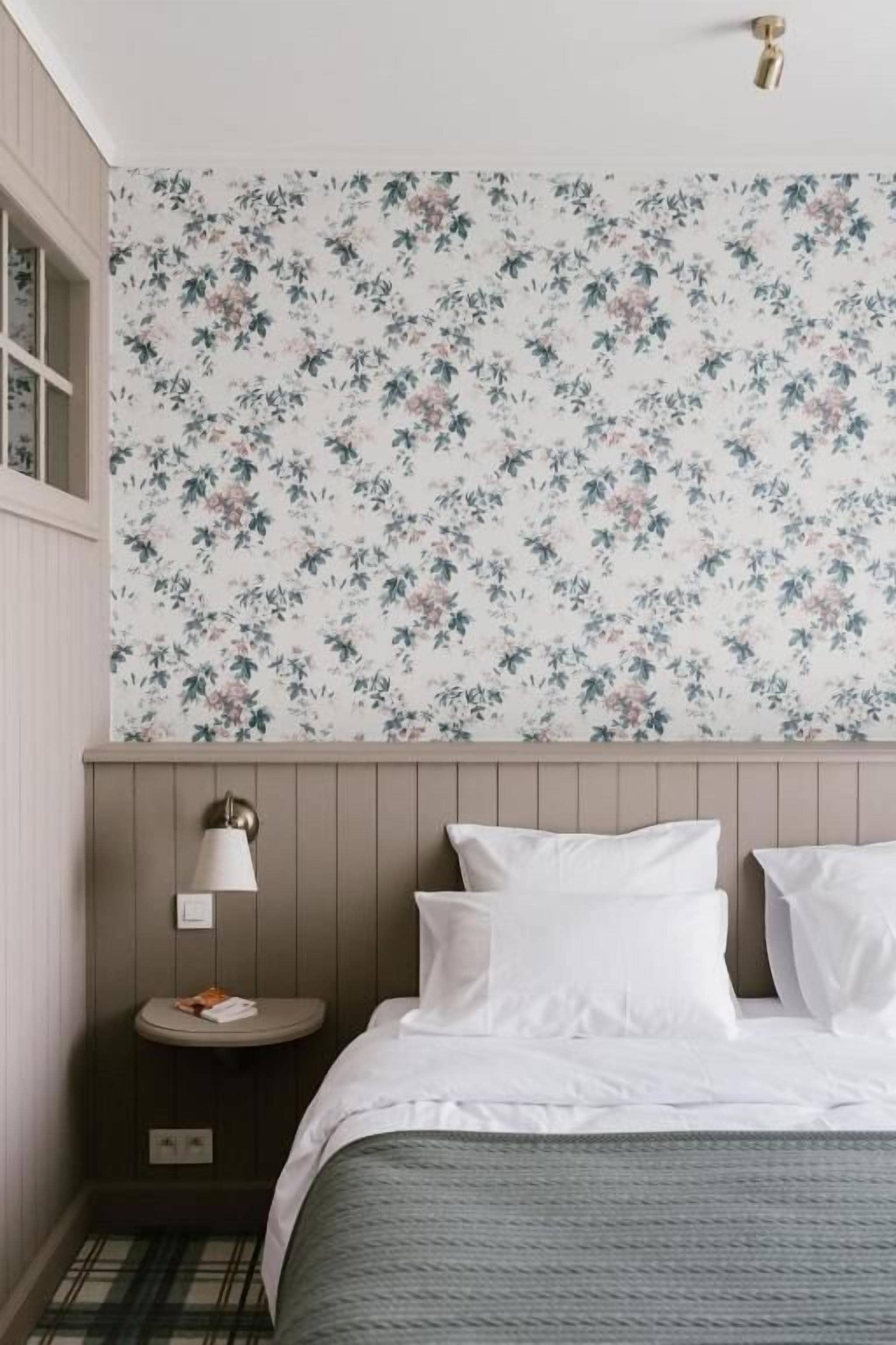 Een slaapkamer met bloemenbehang, een nachtkastje met een lamp en een bed met witte lakens.