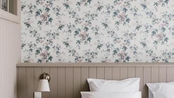 Een slaapkamer met bloemenbehang, een nachtkastje met een lamp en een bed met witte lakens.