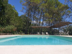 A swimming pool with lounge chairs and a pergola, surrounded by trees.