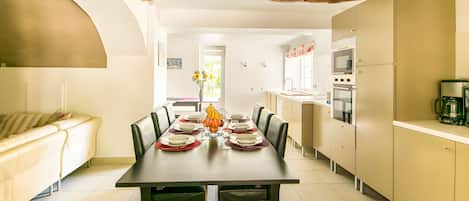 Un comedor con una larga mesa dispuesta para cuatro, una cocina con electrodomésticos modernos y una sala de estar con un sofá.