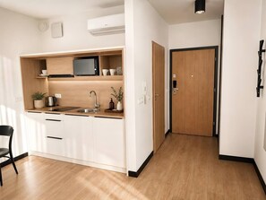 A modern kitchen with white cabinetry, a built-in microwave, and a sink. There is a wooden door leading to another room. - Old Town Heart XXXVI - National Stadium Tower 11 (Warsaw)