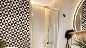 Un baño con pared de diseño geométrico, cabina de ducha de vidrio, inodoro blanco, lavamanos con estructura negra y espejo con estructura negra.