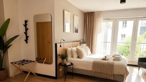 Un dormitorio moderno con una cama grande, piso de madera, un espejo y vista a zonas verdes.
