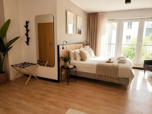 Ein modernes Schlafzimmer mit einem großen Bett, Holzboden, einem Spiegel und Blick auf Grünfläche.