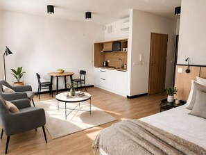 Ein modernes Hotelzimmer mit Bett, Sofa, Esstisch und einer Küchenzeile.