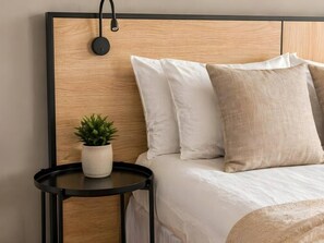 A neatly made bed with white and beige pillows, a small round table with a potted plant, and a wall-mounted lamp. - Old Town Heart – National Stadium Tower 26 (Warsaw)
