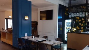 Ein Restaurantinneres mit Tischen, Stühlen, einer Bar und einem mit Getränken gefüllten Kühlschrank.