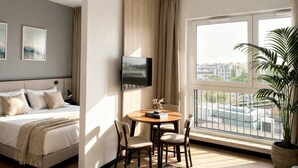 Ein Hotelzimmer mit einem Bett, einem an der Wand montierten Fernseher, einem Esstisch mit Stühlen und einem großen Fenster mit Stadtblick.