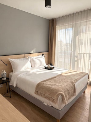Une chambre moderne avec un grand lit, une table de chevet, une lampe et une fenêtre avec des rideaux.