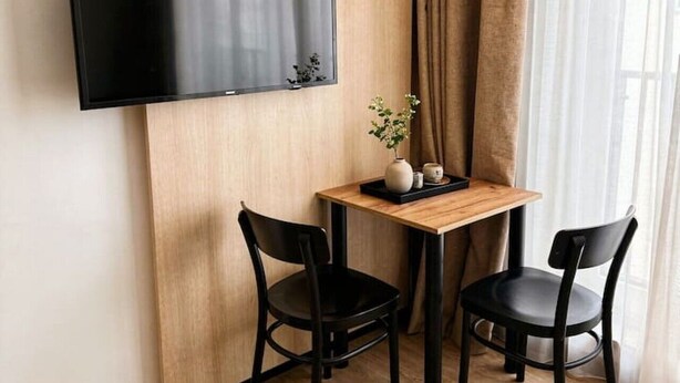 A room with a flat-screen TV mounted on a wooden wall, a small wooden table with two chairs, and a window with curtains. - Old Town Heart - National Stadium Tower 47 (Warsaw)