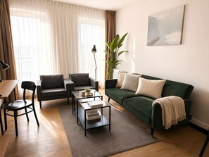 Ein Wohnzimmer mit einem grünen Sofa, einem Couchtisch, einem Sessel und einer Lampe.