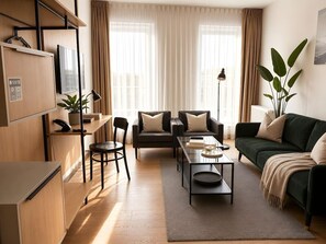 A modern living room with a sofa, armchair, and coffee table. There is a desk with a computer and a plant. The room has large windows with curtains. - Old Town Heart - National Stadium Tower 22 (Warsaw)