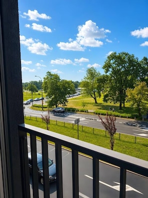 Blick vom Balkon auf eine Straße mit Autos, Bäume und bewölktem Himmel.