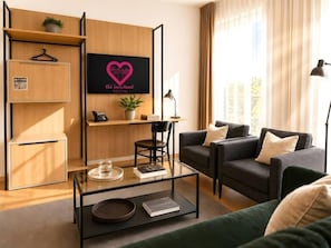 Ein modernes Wohnzimmer mit einer Couch, einem Glastisch und einem an der Wand befestigten Fernseher, der eine herzförmige Grafik zeigt.