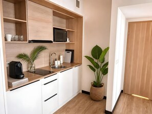 Eine kleine Küche mit weißen Schränken, einer Mikrowelle, einer Kaffeemaschine und einem Blumentopf.