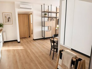 A modern kitchen with wooden flooring, a dining area with a table and chairs, and a built-in shelving unit with a plant. - Old Town Heart-National Stadium Tower 12 (Warsaw)