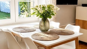 A dining table with four white chairs, a vase with flowers, and woven placemats. - Old Town Heart - XXVII - Brzozowa (Warsaw)