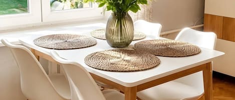 Une table à manger avec quatre chaises blanches, un vase rempli de fleurs et des sets de table en fibres tressées.