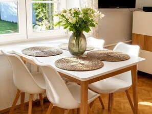 Ett matbord med fyra vita stolar, en vas med blommor och vävda bordstabletter.