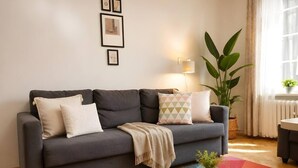 A grey sofa with cushions, a colorful rug, a plant, and a small table with a book and a candle. - Old Town Heart - XXVII - Brzozowa (Warsaw)