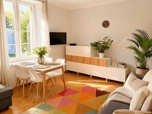 Ein modernes Wohnzimmer mit Essbereich, einem Flachbildfernseher, einer weißen Kommode und einem farbenfrohen Teppich.