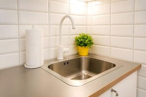 A modern kitchen with a stainless steel sink, white tiles, a white faucet, and a yellow plant. - Old Town Heart - XXVII - Brzozowa (Warsaw)