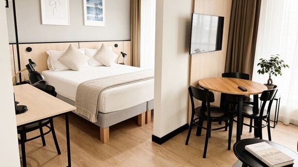 Ett hotellrum med en säng, ett skrivbord, en stol, en tv och ett matbord.
