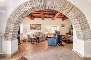 Un salon avec une arche en pierre, un canapé, un fauteuil, une table et une cheminée.