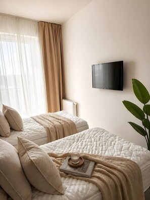 Ein Hotelzimmer mit zwei Betten, einem an der Wand befestigten Fernseher und einem großen Fenster mit Vorhängen.