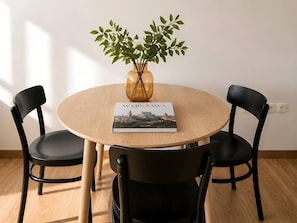 A round wooden table with two black chairs, a vase with green foliage, and a book titled 'Warszawa.' - Old Town Heart - National Stadium Tower 74 (Warsaw)