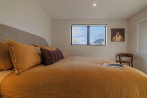 A bedroom with a large bed, a window, a chair, and a painting on the wall. - Modern 1BR Near Christchurch CBD & Cashel Street (Christchurch)
