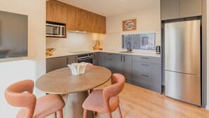 A modern kitchen with a built-in microwave, a stainless steel refrigerator, and a round dining table with chairs. - Modern 1BR Near Christchurch CBD & Cashel Street (Christchurch)