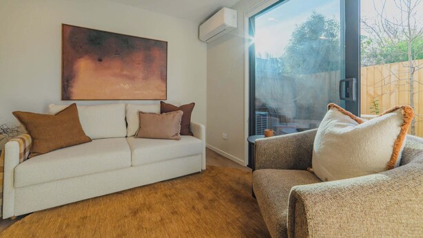 A modern living room with a white sofa, a coffee table, and a large window offering a view of the outdoors. - Modern 1BR Near Christchurch CBD & Cashel Street (Christchurch)
