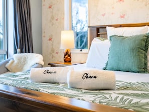 A neatly made bed with two towels labeled 'Ohana' and a nightstand with a lamp. - Spacious 4BR Retreat | Halswell Domain Park & Lake (Christchurch)