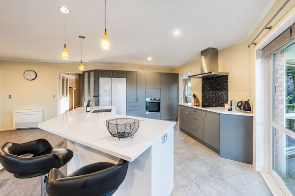 Open-plan kitchen featuring a large island, breakfast bar stools, ample preparation space and a full-size refrigerator.